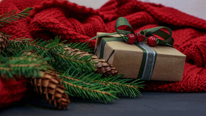 Christmas composition with gift, fir and red knitted blanket on dark background. Christmas poster or banner