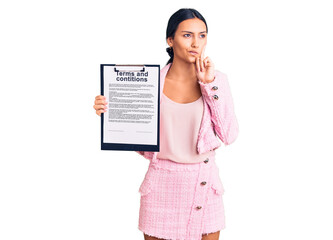 Poster - Young beautiful latin girl holding clipboard with terms and conditions document serious face thinking about question with hand on chin, thoughtful about confusing idea