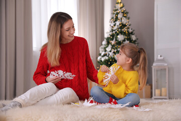 Canvas Print - Happy mother and daughter making paper snowflakes near Christmas tree at home