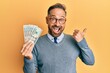 © Krakenimages.com - Handsome middle age man holding 20 dollars banknotes pointing thumb up to the side smiling happy with open mouth
