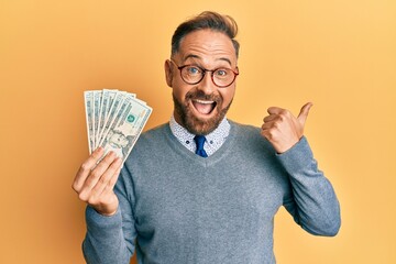 Poster - Handsome middle age man holding 20 dollars banknotes pointing thumb up to the side smiling happy with open mouth