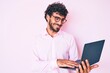 © Krakenimages.com - Handsome young man with curly hair and bear working using computer laptop looking positive and happy standing and smiling with a confident smile showing teeth