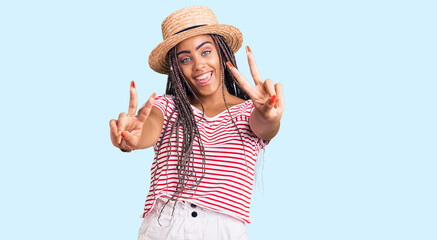 Sticker - Young african american woman with braids wearing summer hat smiling with tongue out showing fingers of both hands doing victory sign. number two.