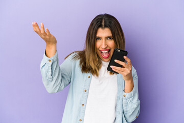 Wall Mural - Young indian woman holding a phone isolated receiving a pleasant surprise, excited and raising hands.