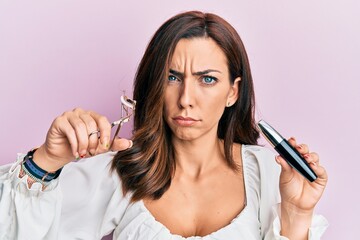 Wall Mural - Young brunette woman holding eyelash curler skeptic and nervous, frowning upset because of problem. negative person.