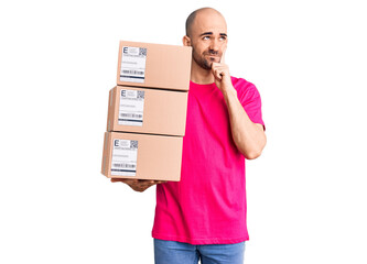 Wall Mural - Young handsome man holding delivery package serious face thinking about question with hand on chin, thoughtful about confusing idea