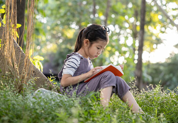 A pretty little Asian girl reading a book under the big tree.