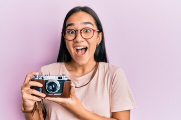 Sticker - Young asian woman holding vintage camera celebrating crazy and amazed for success with open eyes screaming excited.