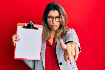 Canvas Print - Beautiful brunette woman holding clipboard with blank space skeptic and nervous, frowning upset because of problem. negative person.