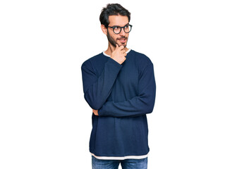 Wall Mural - Young hispanic man wearing casual clothes and glasses with hand on chin thinking about question, pensive expression. smiling with thoughtful face. doubt concept.