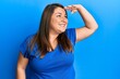 © Krakenimages.com - Beautiful brunette plus size woman wearing casual blue t shirt very happy and smiling looking far away with hand over head. searching concept.