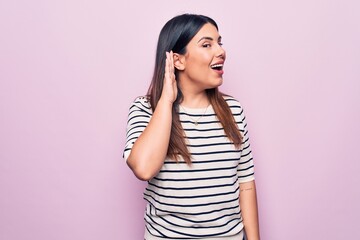 Canvas Print - Young beautiful brunette woman wearing casual striped t-shirt over isolated pink background smiling with hand over ear listening and hearing to rumor or gossip. Deafness concept.