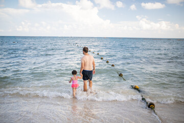 Father and young daughter holding hands as they walk on the beach