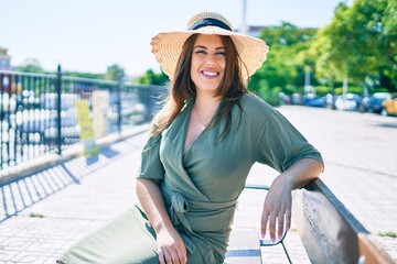 Wall Mural - Young hispanic woman on vacation smiling happy sitting on bench at street of city