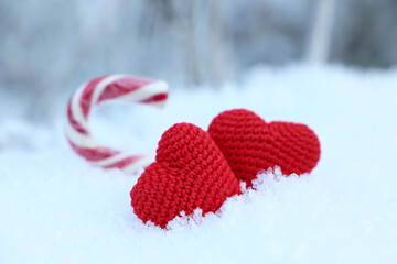 Wall Mural - Two love hearts and Christmas candy cane on a snow in winter forest. Red knitted symbols of Valentine's day, background for New Year holiday