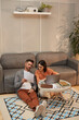 © Seventyfour - Vertical high angle portrait of modern adult couple working from home together while sitting on floor in stylish interior and using laptop, copy space