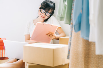 Young Asian businesswoman is sitting on the floor to check her orders from e-commerce sites