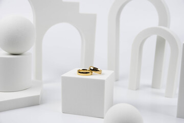 Golden wedding rings on trendy white podium. Aesthetic still life art photography.