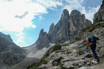 a woman with big backpack and sticks, hiking in high italian dolomites. there are many sharp peaks i