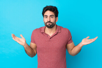 Wall Mural - Young handsome man with beard over isolated blue background making doubts gesture