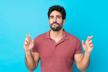 Wall Mural - Young handsome man with beard over isolated blue background with fingers crossing and wishing the best