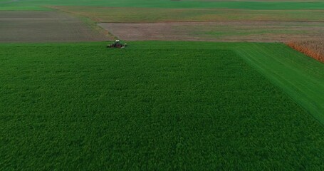 Wall Mural - Aerial drone view of tractor cutting green grass on farming field. Harvesting for bale hay for livestock. Farmland in Slovenia. Agriculture harvesting and agronomy concept. Backward moving