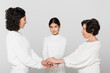 © LIGHTFIELD STUDIOS - Hispanic girl holding hands with mother and granny isolated on grey, three generations of women