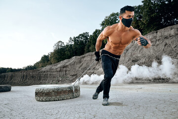 Sportsman in black mask using heavy tyre for workout