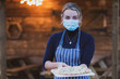© Mint Images - Woman waitress in apron and face mask holding plate of pizza.