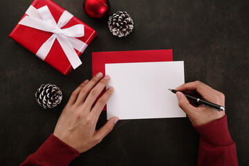 Wall Mural - hands writing white greeting card mockup with christmas decoration on grunge background.