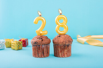 28 Number gold candle on a cupcake against a pastel blue background twenty eight year celebration