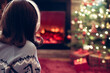 © flowertiare - Woman in headphones sitting and warming at winter evening near fireplace flame and  christmas tree.