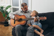 © cherryandbees - boy with his grandfather playing guitar at home
