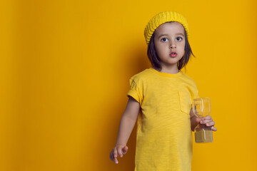 boy child in a yellow t shirt and a knitted hat on the background in the Studio holding an hourglass