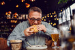 © dusanpetkovic1 - Middle aged bearded hungry man sitting in restaurant and eating delicious burger.