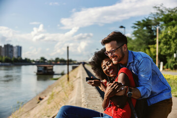 Young happy multiracial couple hugging outdoors by the river.