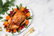 Christmas oven roasted duck on a white plate decorated with cranberries, pomegranate, persimmon, rosemary and sage. Marble background. Copy space. Chrismas food concept. 