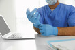 © New Africa - Doctor putting on medical gloves at table in office, closeup