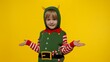 © Andrii Iemelianenko - Side view shocked blonde kid girl in Christmas elf Santa helper costume. Child turn round look at camera and say ask question what isolated on yellow background. People sincere emotions