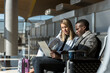 © David Prado/Stocksy - multiracial coworkers sitting at the airport working on his laptop and tablet waiting for the flight