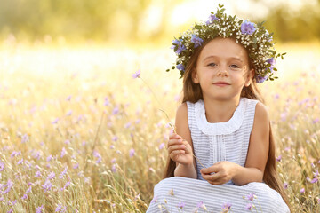 Cute little girl wearing flower wreath outdoors, space for text. Child spending time in nature