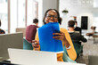 © David Prado/Stocksy - Positive woman laughing while working with laptop and documents at office