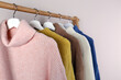 © New Africa - Warm sweaters hanging on wooden rack against light background, closeup