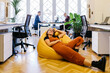 © JOSEP M ROVIROSA/Westend61 - Smiling businesswoman resting on bean bag in office
