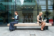 © PETE  MULLER/Westend61 - Businesswoman and colleague working while sitting with social distance on bench against office building exterior