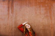 Young Woman With Eyes Closed Leaning On Brown Wall