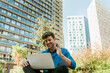 © VALENTINA BARRETO STUDIO/Westend61 - Happy young businessman waving hand while video calling through laptop against modern buildings