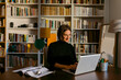 © VALENTINA BARRETO STUDIO/Westend61 - Smiling businesswoman working on laptop sitting against bookshelf at home