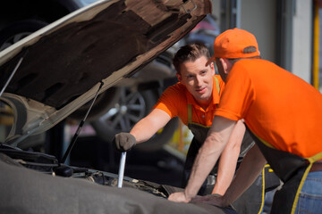 Two men are car mechanic Use a wrench and a cord to check the car battery.