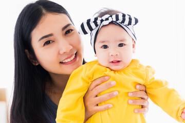 Portrait of beautiful young Asian mother playing and smiling together with his newborn little baby at home, Parent mom and little kid relaxing in the bedroom, Family having fun together